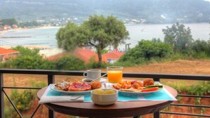Ein Frühstückstisch mit Croissants, Toast, Obst und Saft, mit Blick auf einen malerischen See und Berge.