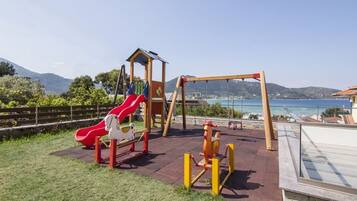Children can play on the slide, climbing structure, and swing set in this outdoor play area with a view of the surrounding water and hills.