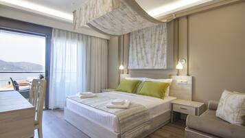 A hotel room with a bed, a desk, a chair, a sofa, and a view of the sea.