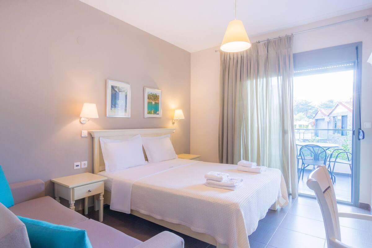 Une chambre d’hôtel avec un lit, une table de chevet, une chaise, une table et un balcon avec vue.