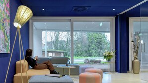A modern waiting area with seating, a lamp, and a view of the outdoors. - Hotel Eastside (St. Gallen)