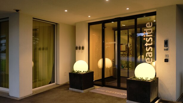 A hotel entrance with glass doors, two illuminated spherical decorations, and a sign reading "hotel eastside." - Hotel Eastside (St. Gallen)