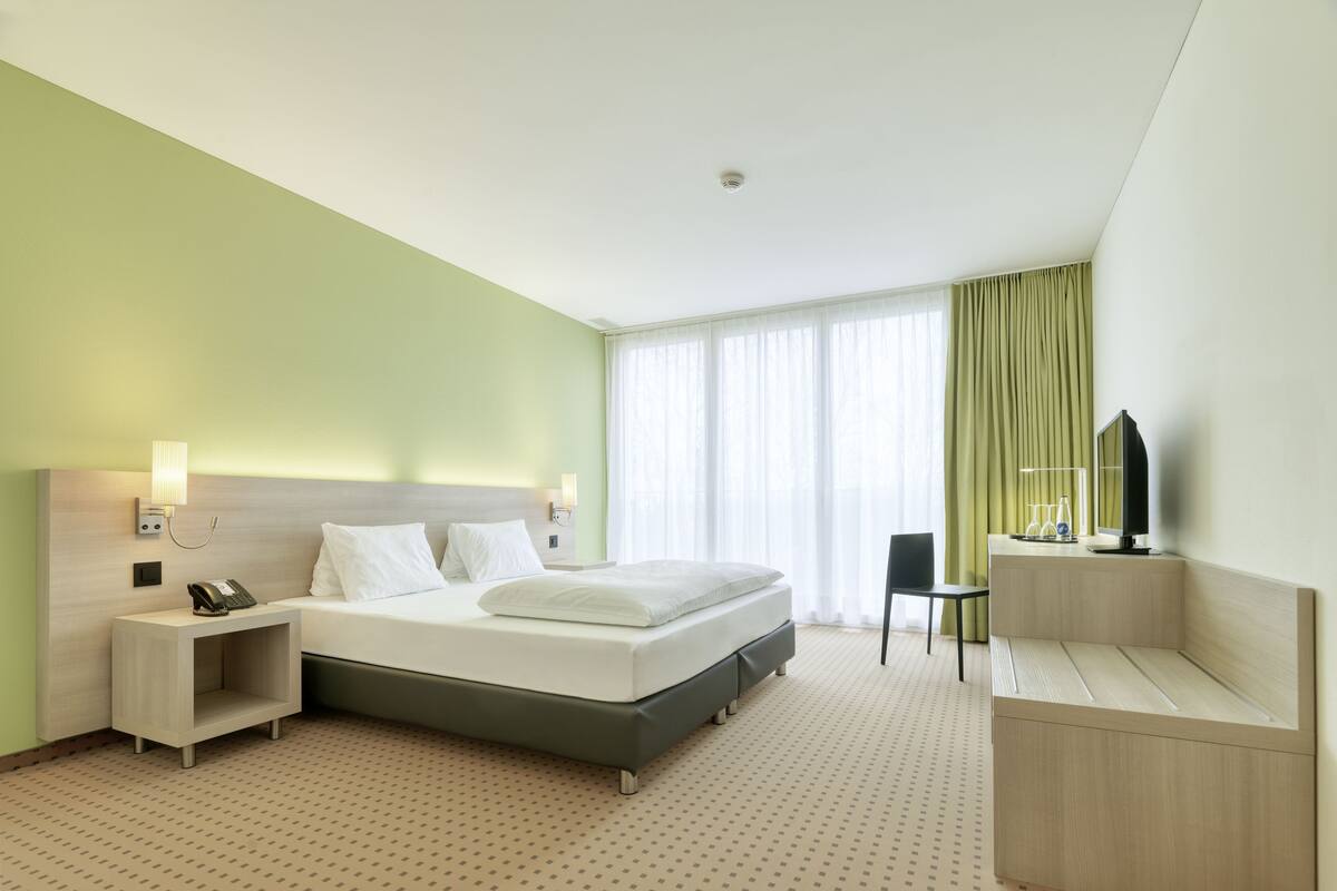 A modern hotel room with a large bed, bedside tables, a desk with a chair, and a television.
