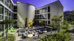A modern building with a curved exterior, outdoor seating area with green chairs and yellow umbrellas, and a pool. - Hotel Eastside (St. Gallen)