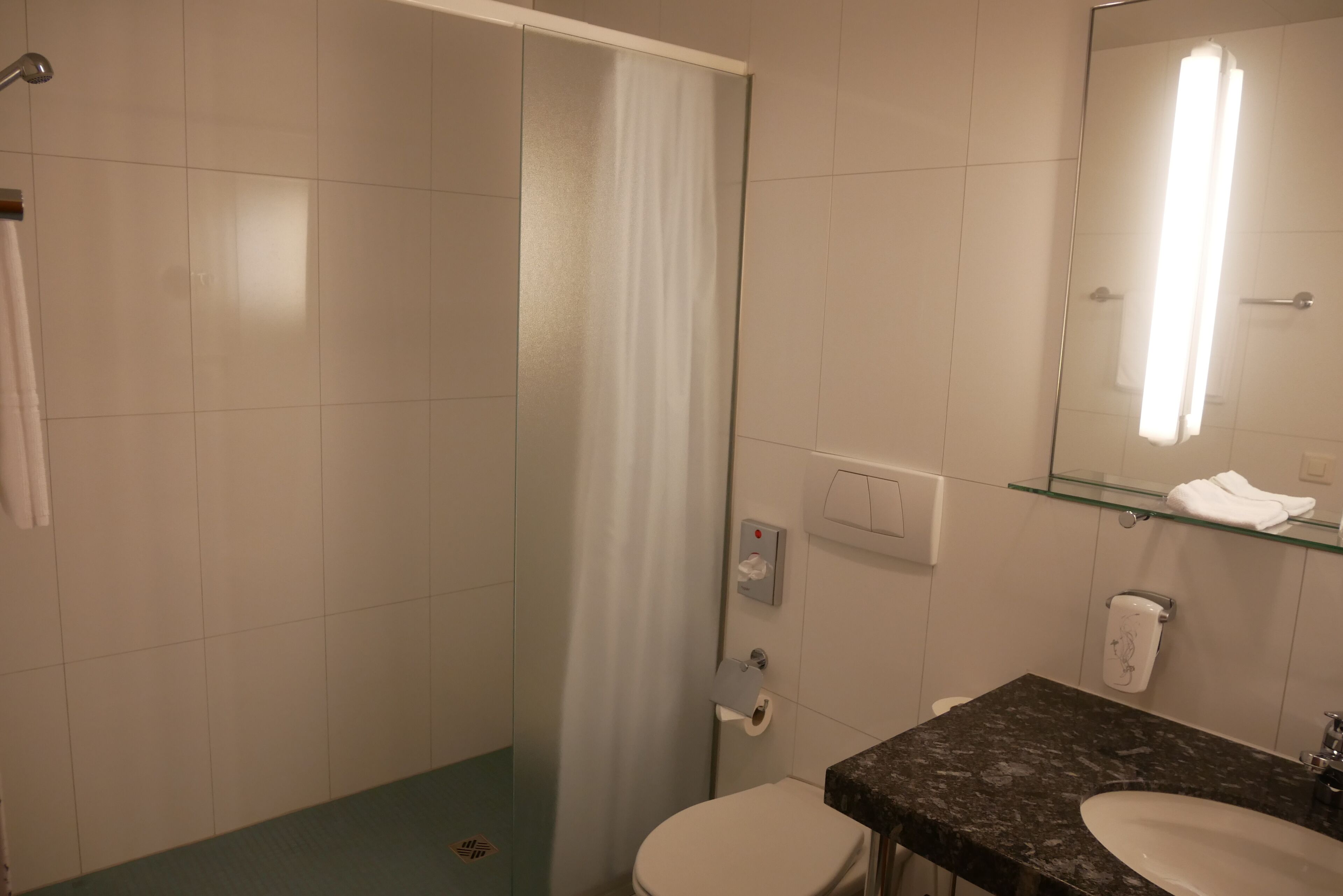 A bathroom with a shower, toilet, sink, and a glass shelf with a towel.