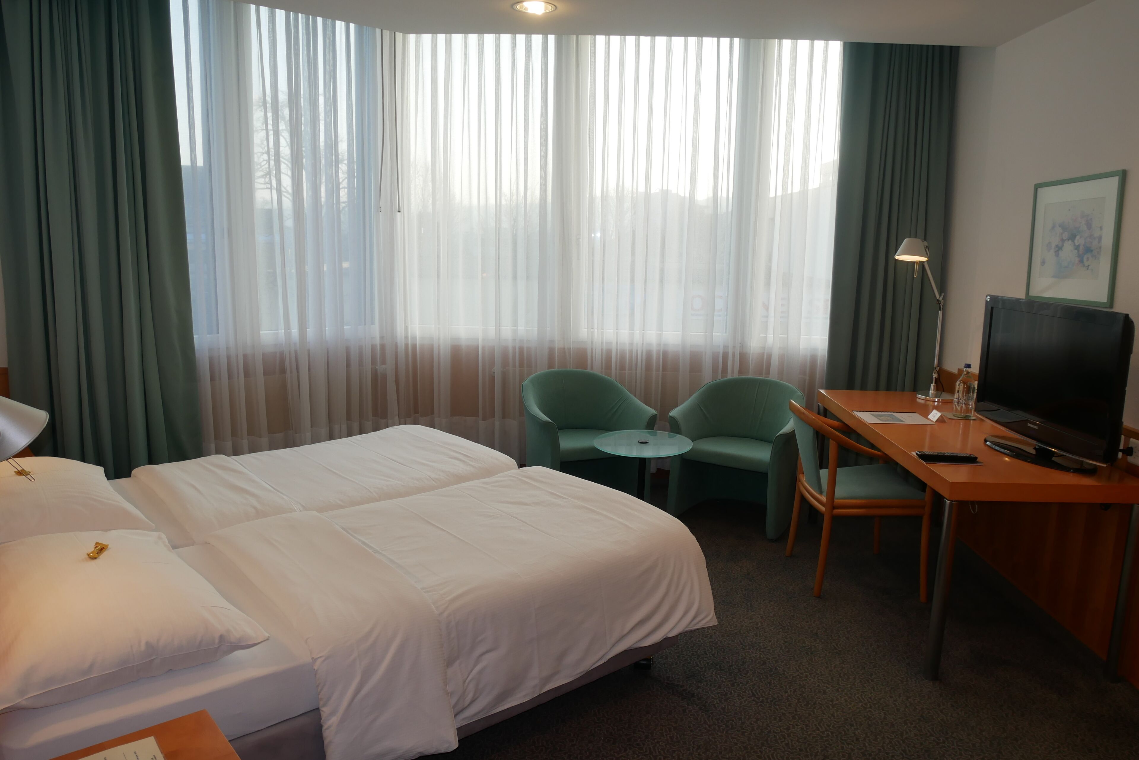 A hotel room with two beds, a desk with a TV, a lamp, and a chair.
