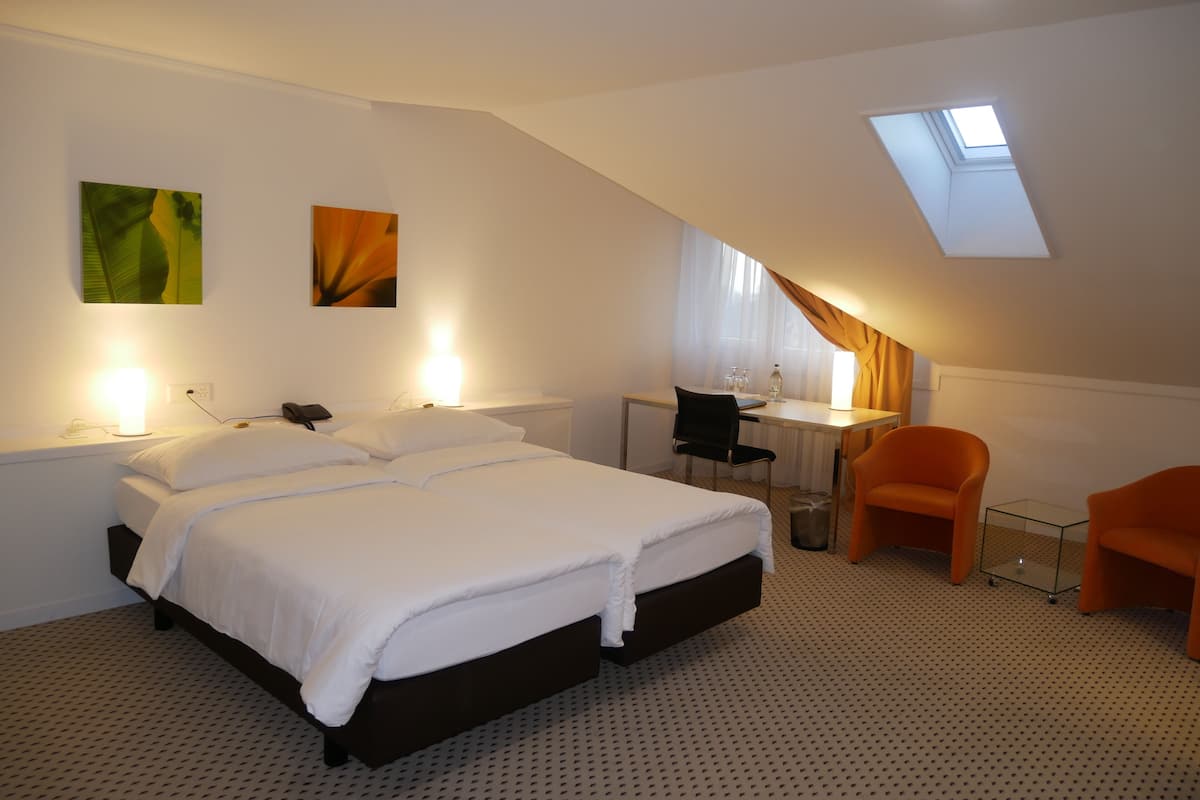 A bedroom with a bed, a desk, two chairs, a small table, and a skylight.