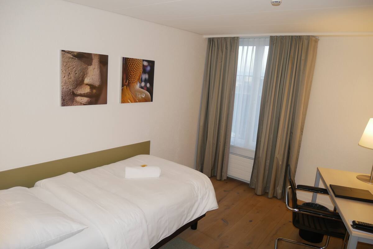 A hotel room with a bed, a desk, a chair, and two wall-mounted pictures.