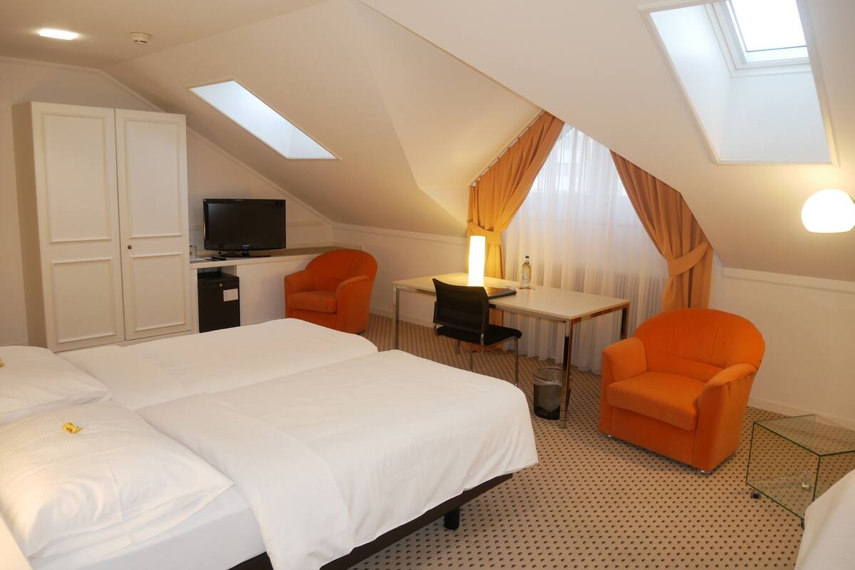 A hotel room with two beds, a desk, a chair, a TV, and a window with curtains.