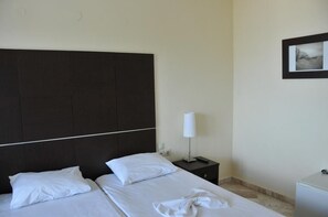 A hotel room with a dark headboard, two beds with white linens, a bedside table with a lamp, and a small white cabinet. - Sunrise Beach (Thasos)