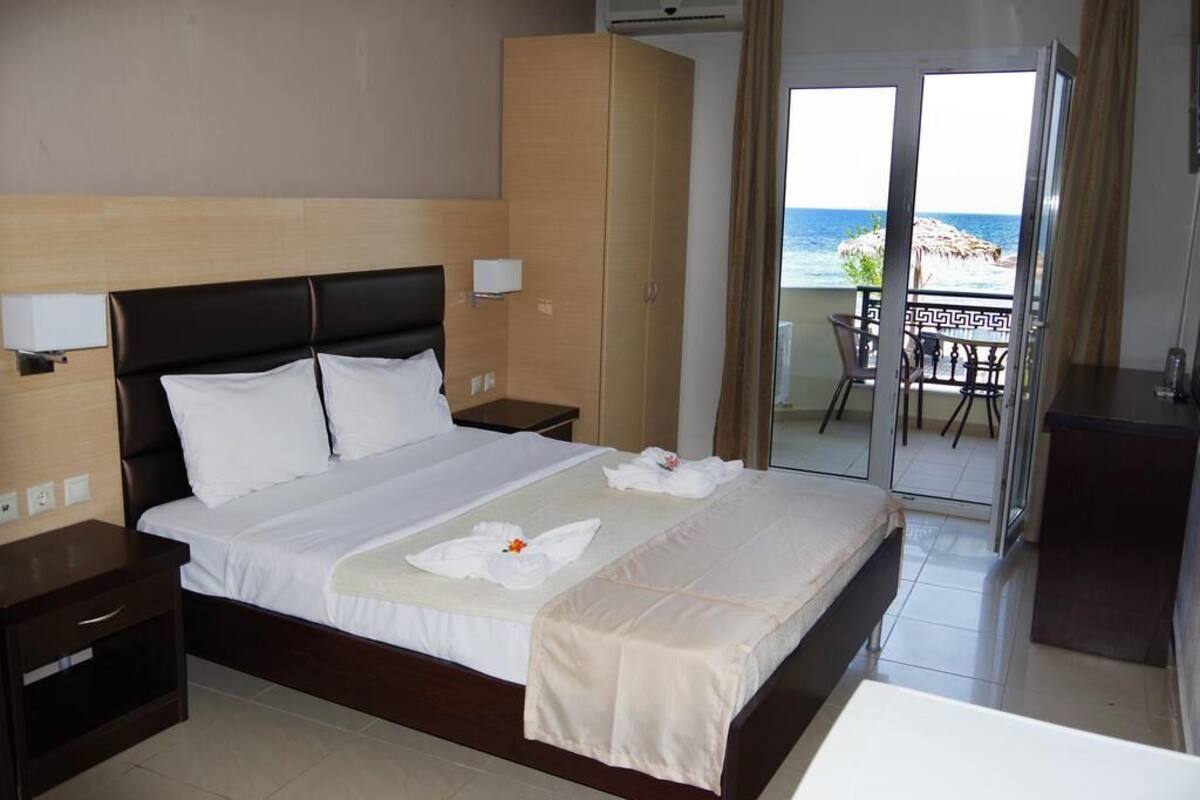 Ein Hotelzimmer mit einem großen Bett, einem Kleiderschrank, einem Nachttisch und einem Balkon mit Meerblick.