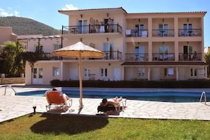 A multi-story hotel with a swimming pool, outdoor seating, and a mountain backdrop. - Sunrise Beach (Thasos)