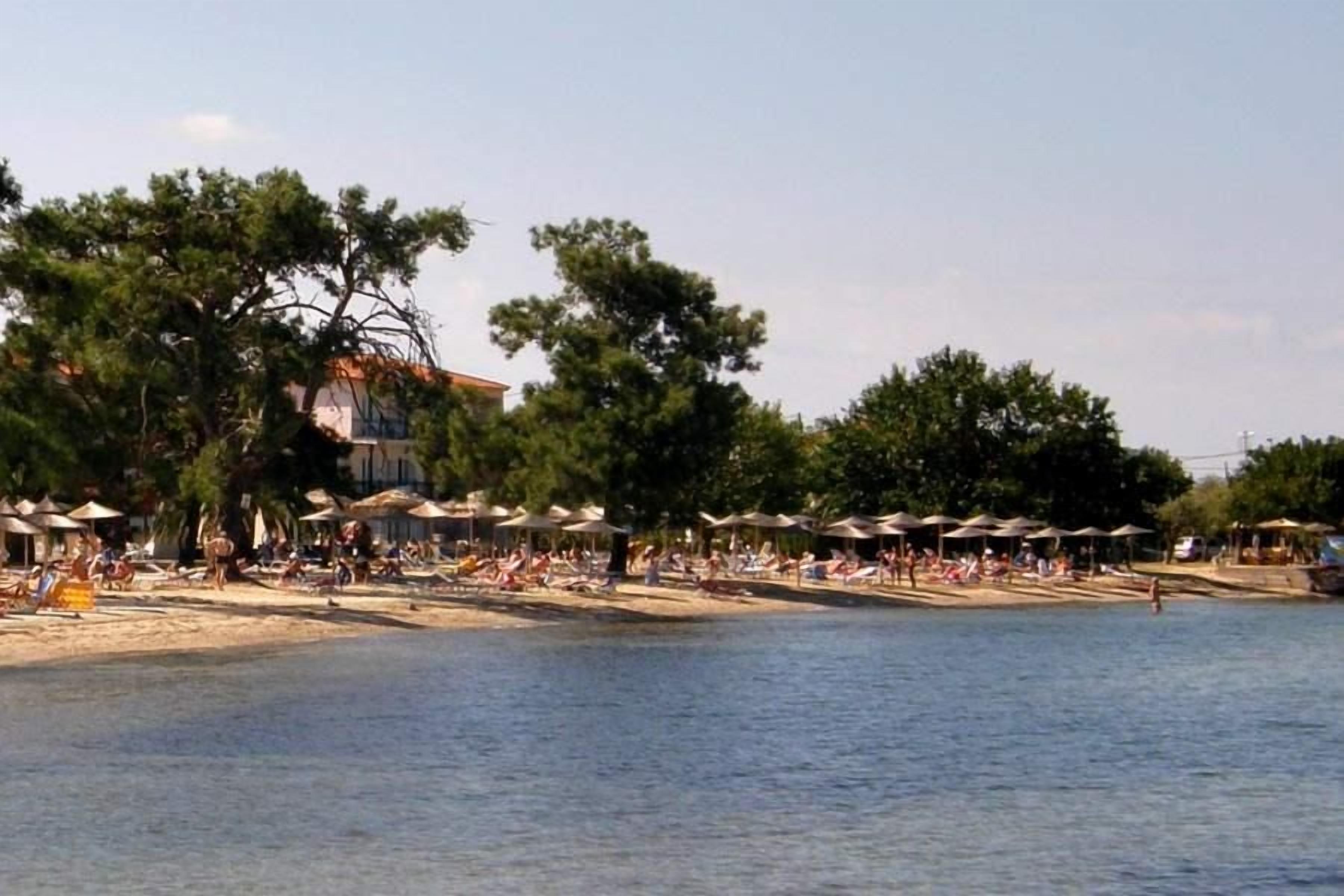 A beach with umbrellas and people, a building in the background, and trees.