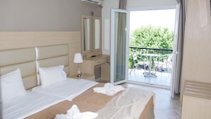A hotel room with a large bed, a desk, a chair, and a balcony with outdoor furniture. - Sunrise Beach (Thasos)