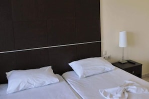 A hotel room with a dark headboard, two beds with white linens, and a bedside table with a lamp. - Sunrise Beach (Thasos)