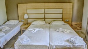 A hotel room with two single beds, a wooden headboard, a bedside table with a lamp, and a tiled floor. - Sunrise Beach (Thasos)