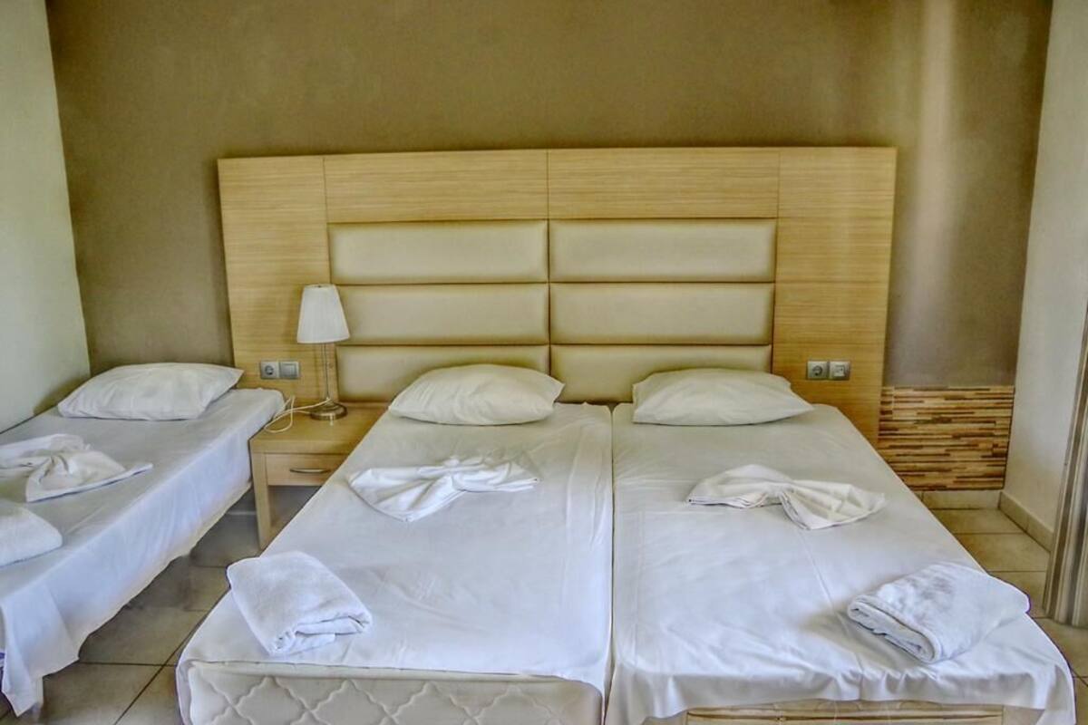 Ein Hotelzimmer mit zwei Einzelbetten, einem Holzkopfteil, einem Nachttisch mit Lampe und einem gefliesten Boden.