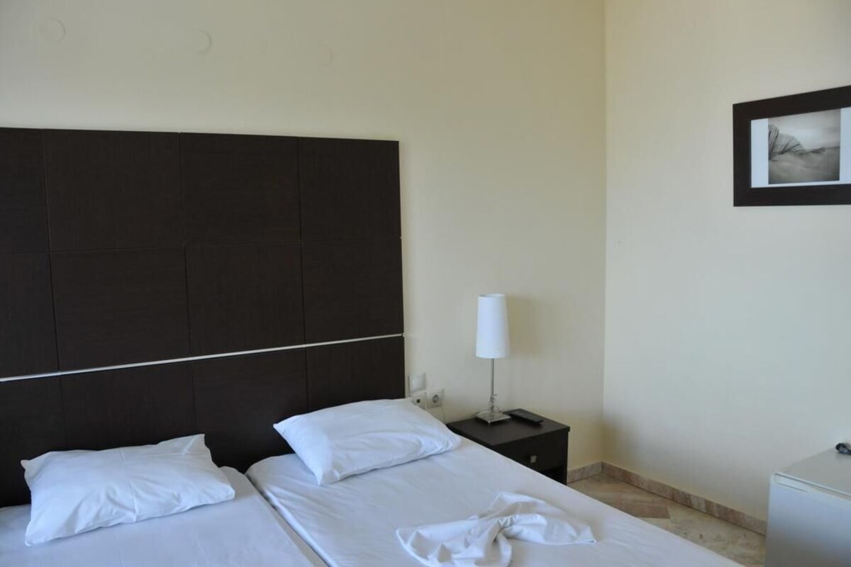 A hotel room with a dark headboard, two beds with white linens, a bedside table with a lamp, and a small white cabinet.