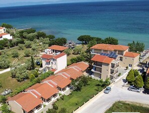 A coastal residential area with multiple two-story buildings, some with balconies, and a road with cars. - Sunrise Beach (Thasos)