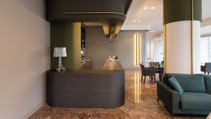 Un comptoir d’accueil au design incurvé, un espace détente avec un canapé et une table à manger dans un hall d’entrée moderne.