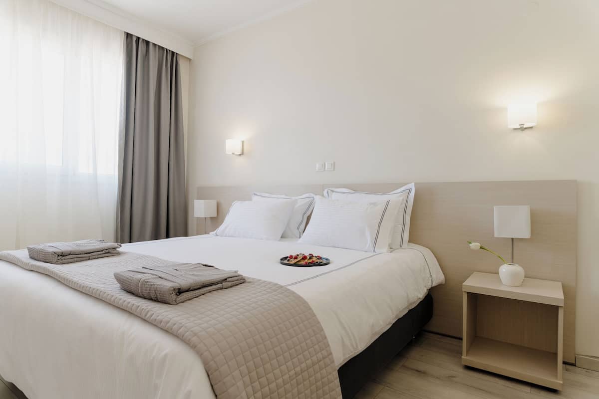 A hotel room with a bed, a nightstand, a lamp, and a window with curtains.