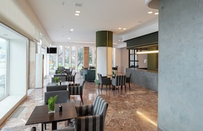 Un hall d’hôtel moderne, doté d’un espace salon, d’un comptoir d’accueil et de grandes fenêtres.