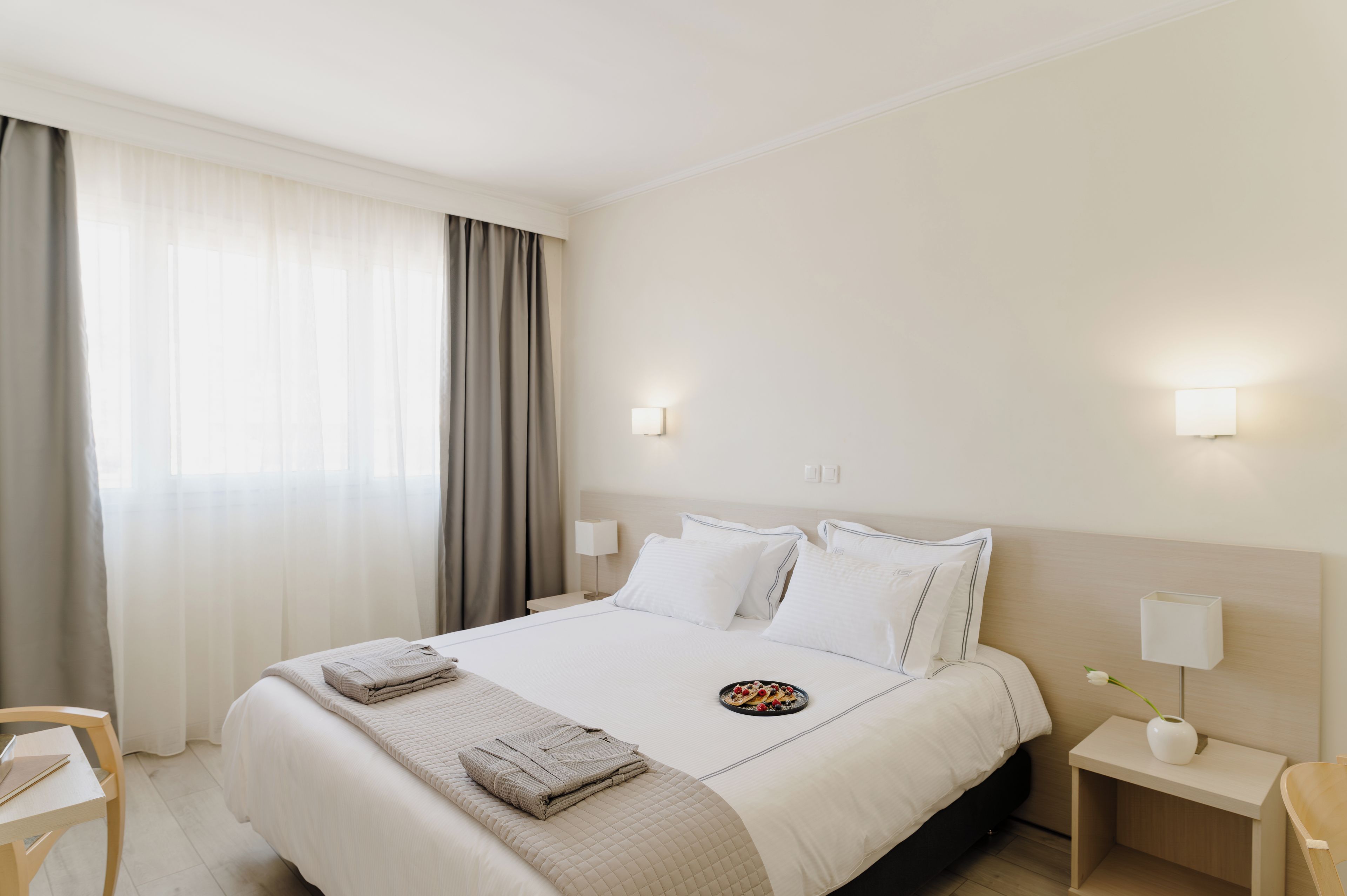 Une chambre d’hôtel avec un grand lit, une table de chevet, une chaise et une fenêtre avec des rideaux.