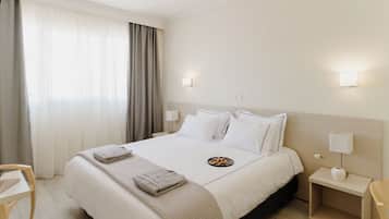 Une chambre d’hôtel avec un grand lit, une table de chevet, une chaise et une fenêtre avec des rideaux.