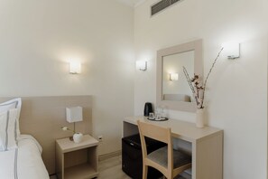 A hotel room with a bed, bedside table with a lamp, a desk with a mirror, a chair, and a small cabinet. - Nestos (Xanthi)