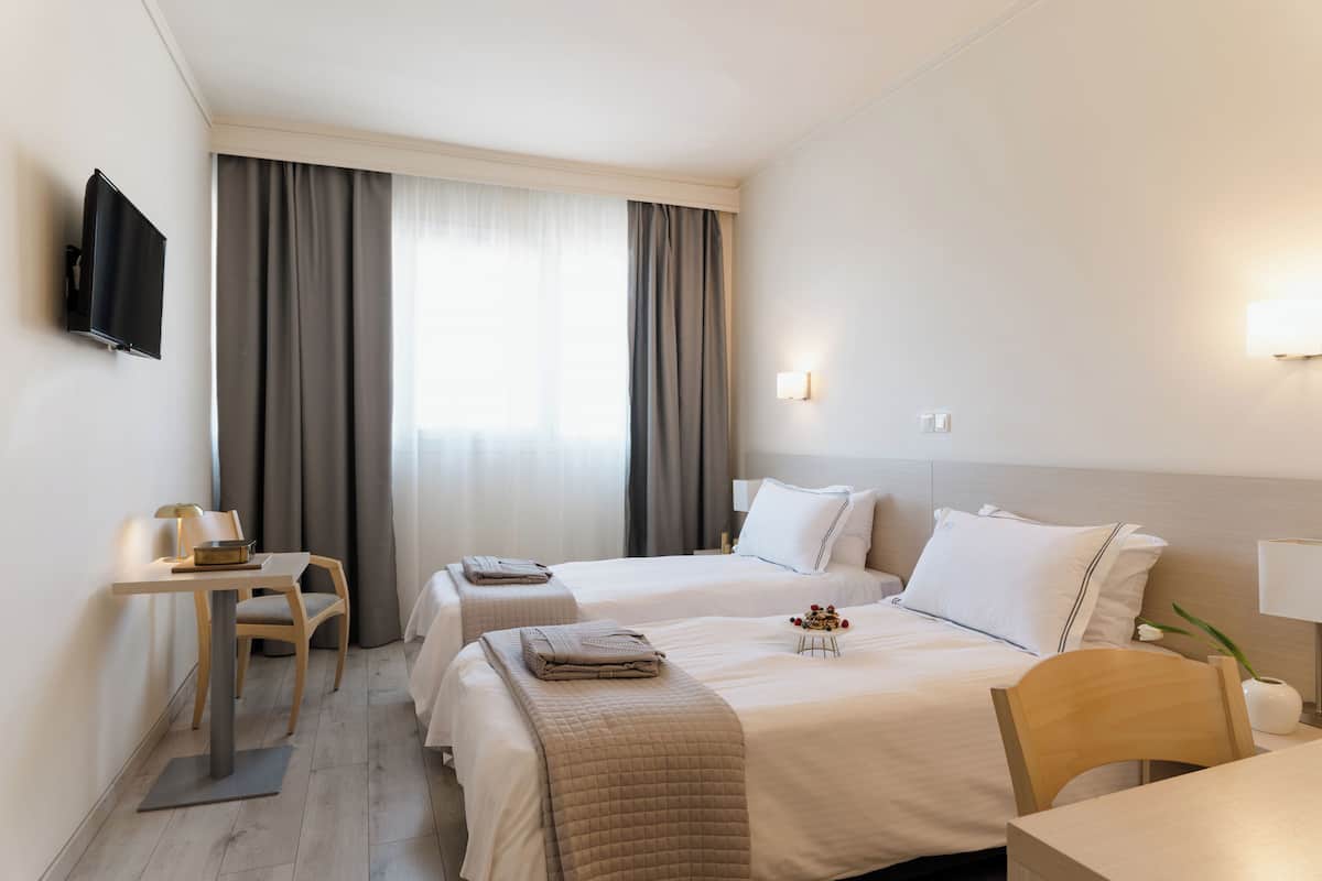 A hotel room with two beds, a desk, a chair, a TV, and a window with curtains.