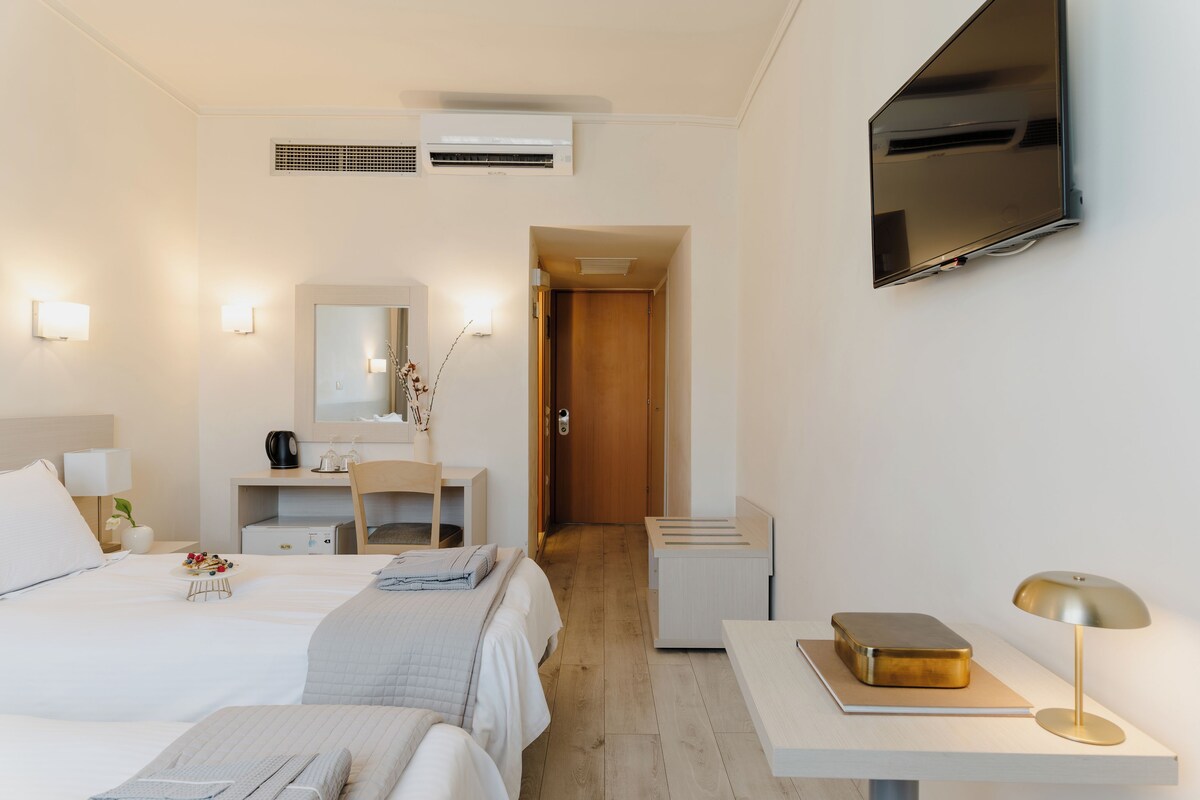 Una habitación de hotel con cama, mesita de noche, lámpara, televisor y escritorio con silla.