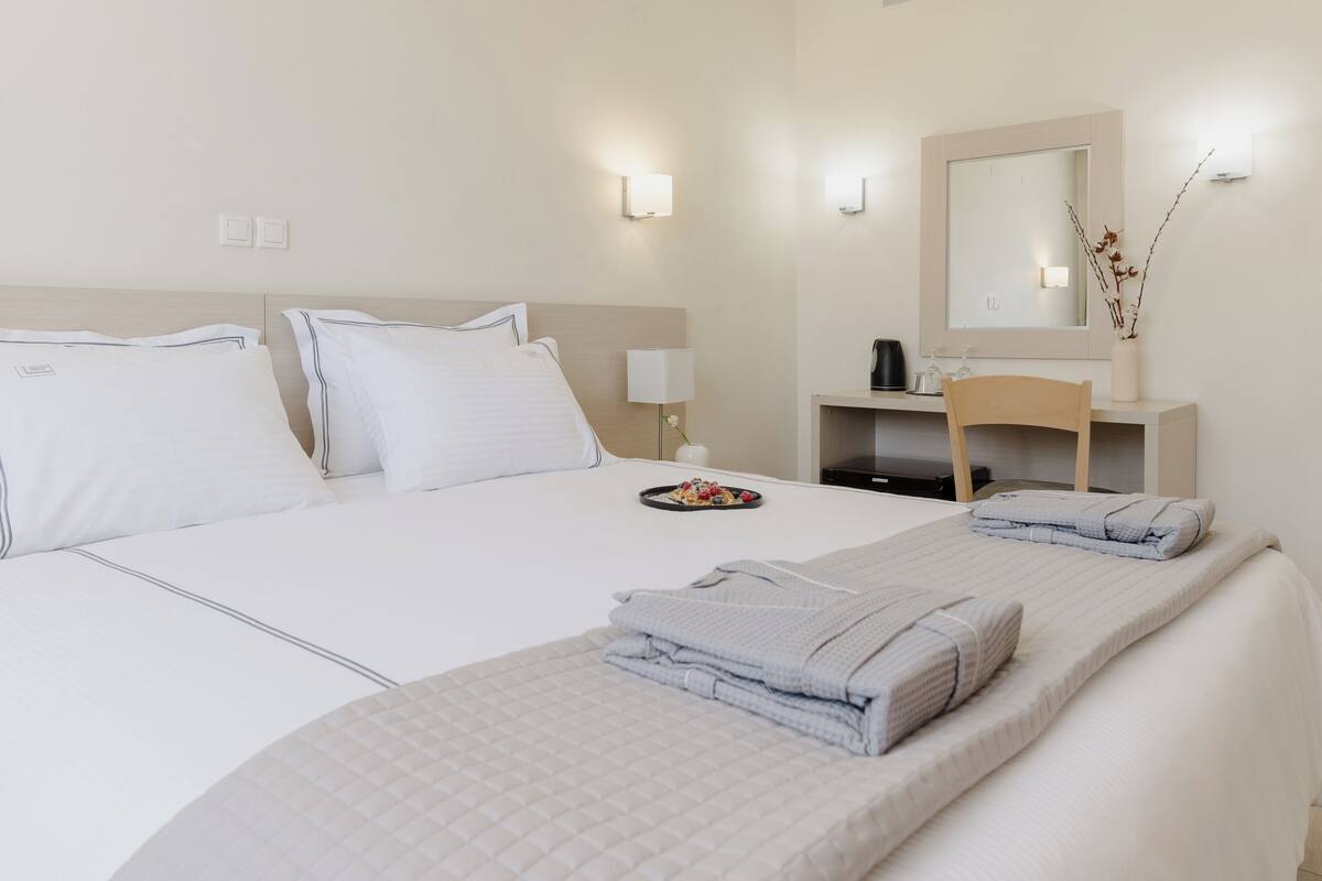 A hotel room with a bed, a nightstand, a mirror, and a small table with a vase.