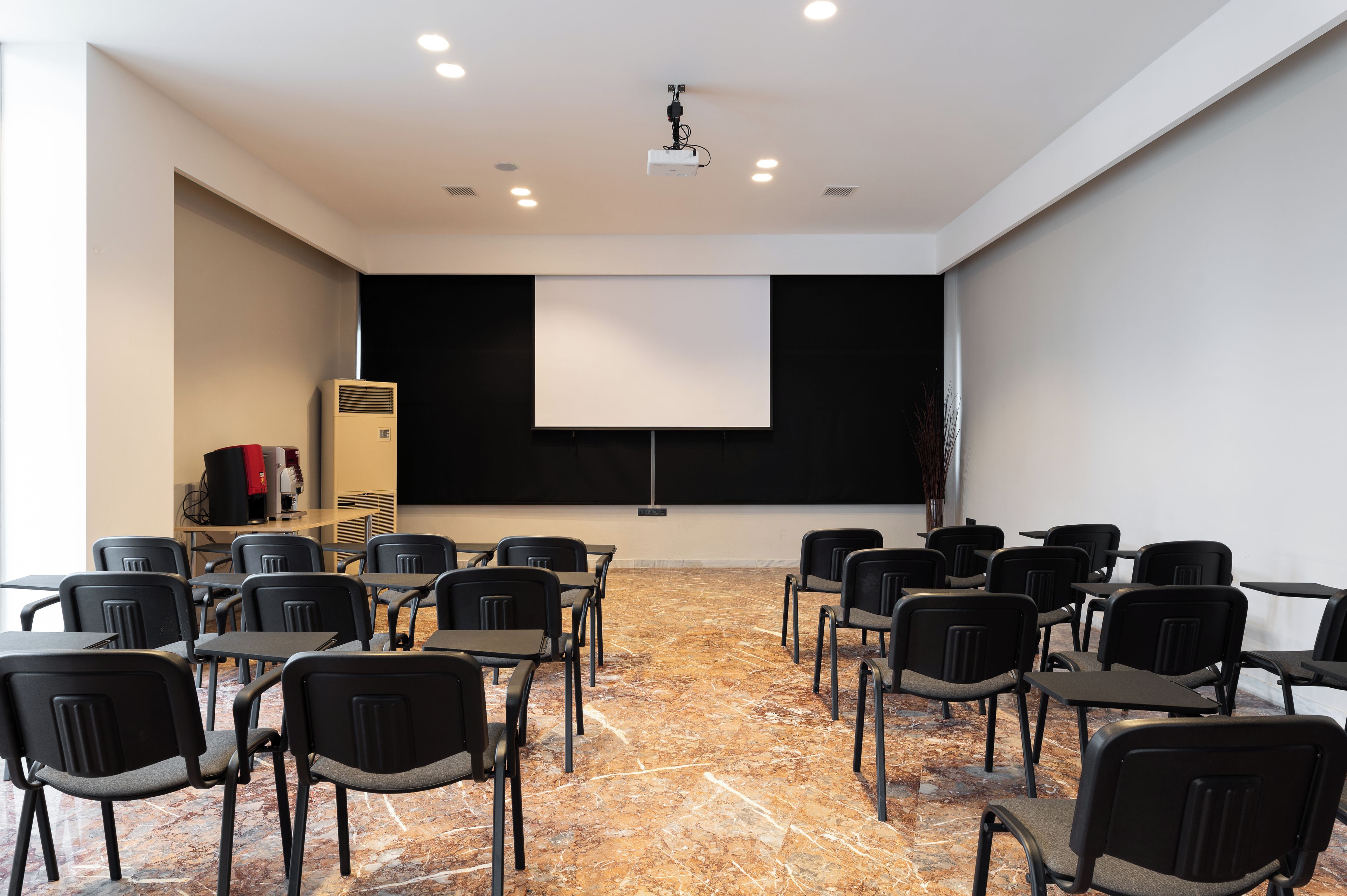 Un salón de conferencias con proyector, pantalla y filas de sillas.