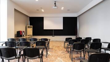Un salón de conferencias con proyector, pantalla y filas de sillas.