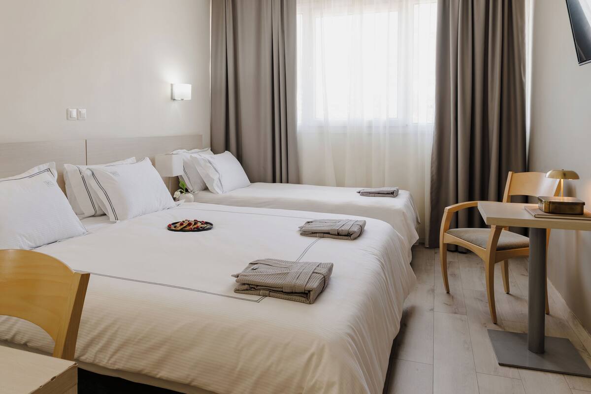A hotel room with two beds, a desk, a chair, and a window with curtains.