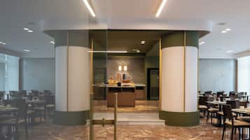 A modern hotel lobby with a central reception desk, marble flooring, and glass partitions.
