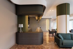 En receptionsdisk med en böjd design, en sittgrupp med en soffa och ett matbord i en modern lobby.