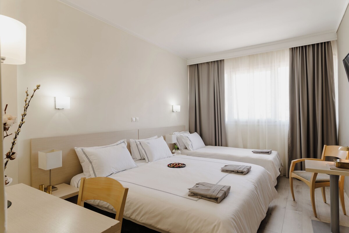 Habitación de hotel con dos camas, un escritorio, una silla y una lámpara.