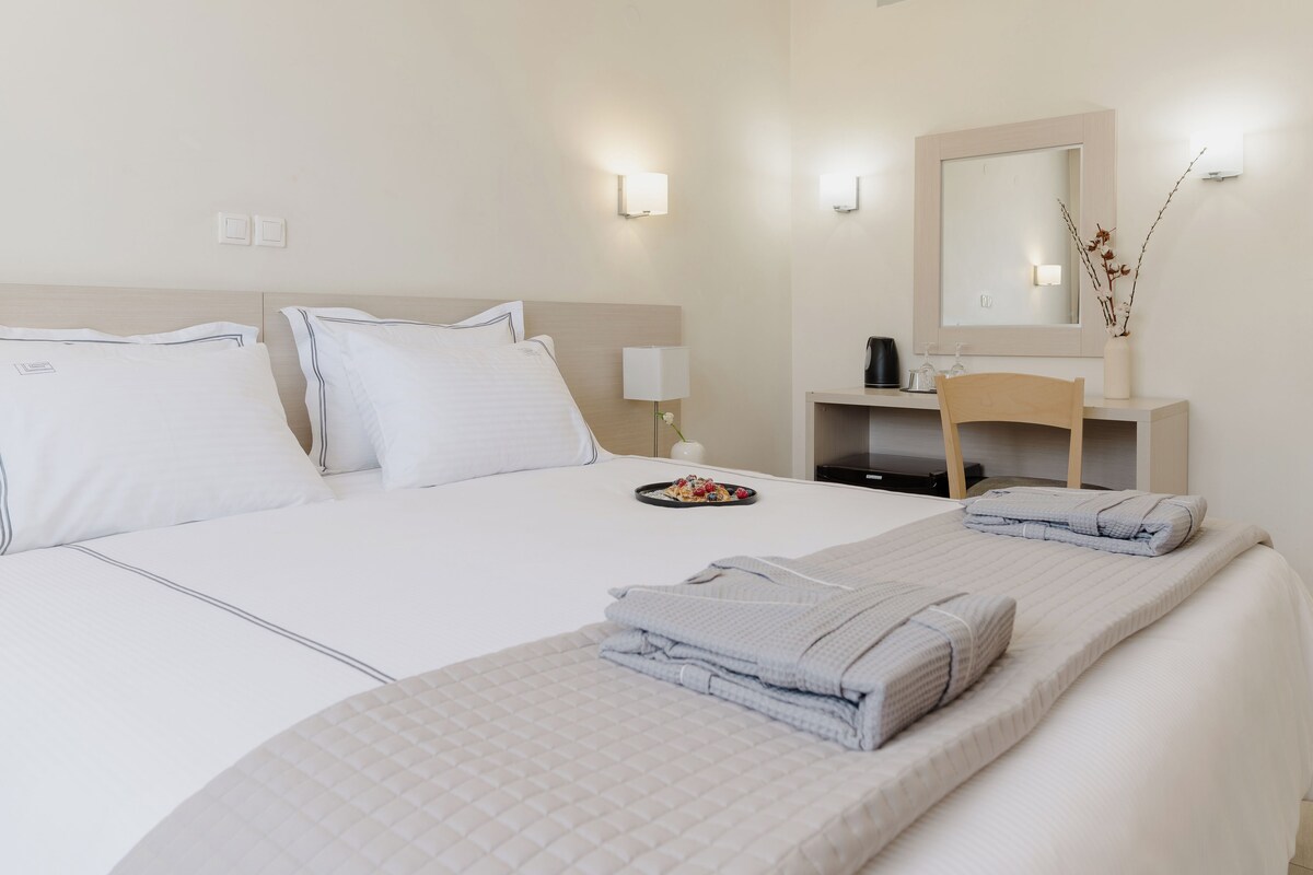 Una habitación de hotel con cama, mesita de noche, espejo y una pequeña mesa con un florero.