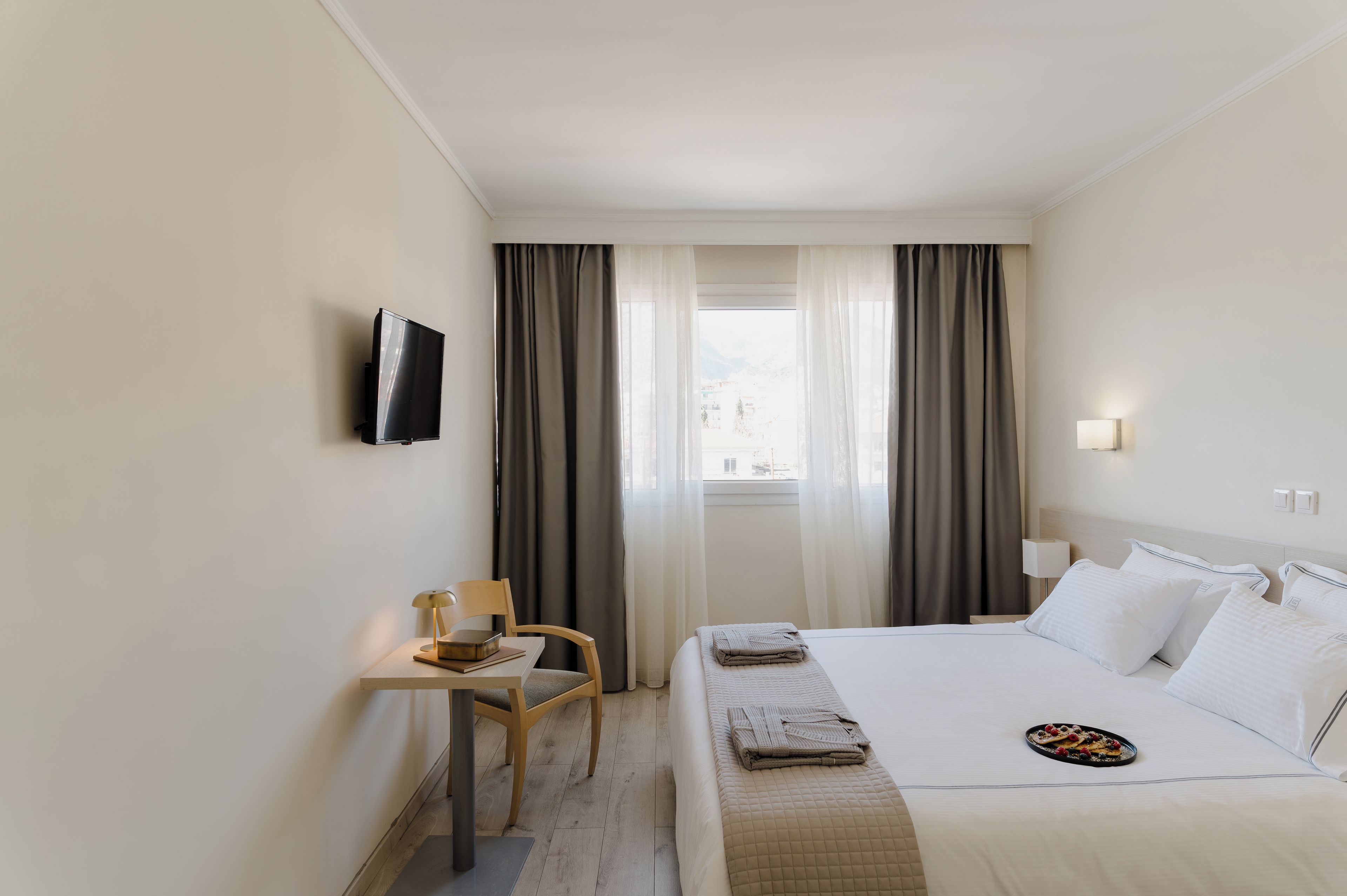 A hotel room with a bed, a desk, a chair, a TV, and a window with curtains.