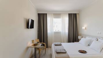 A hotel room with a bed, a desk, a chair, a TV, and a window with curtains.