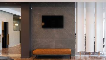 Um lobby moderno com piso de mármore, um banco, uma TV de tela plana fixada em uma parede de mármore e um painel de vidro.
