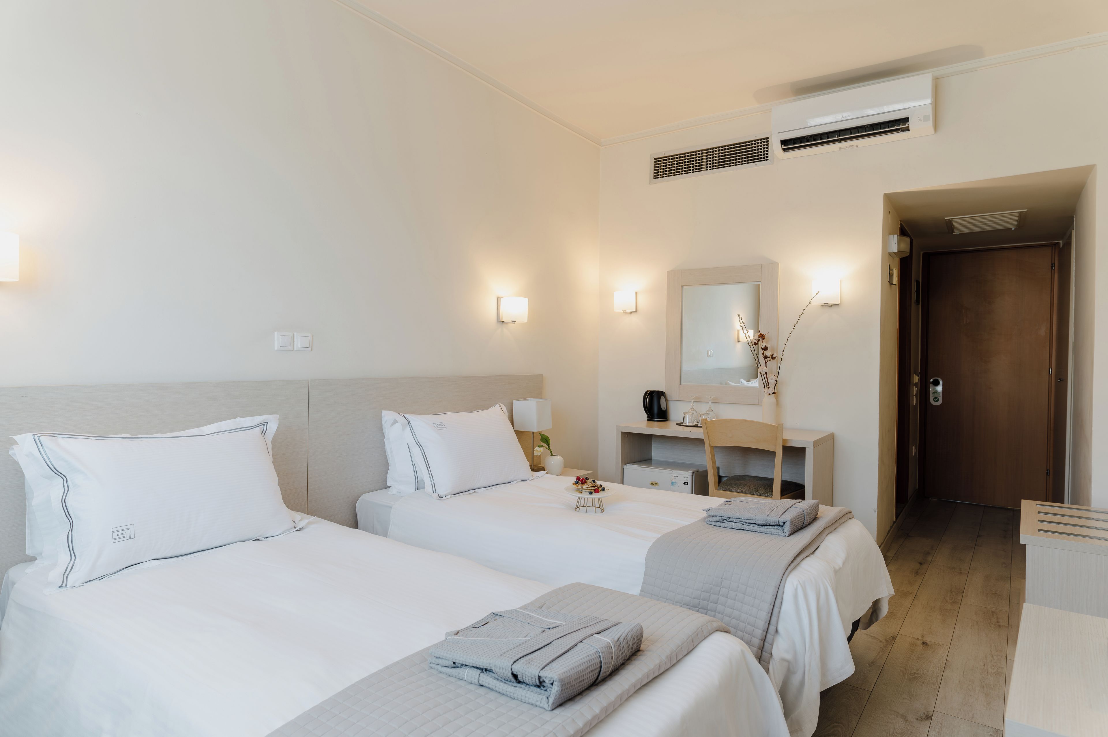A hotel room with two beds, a desk, a mirror, and a door.
