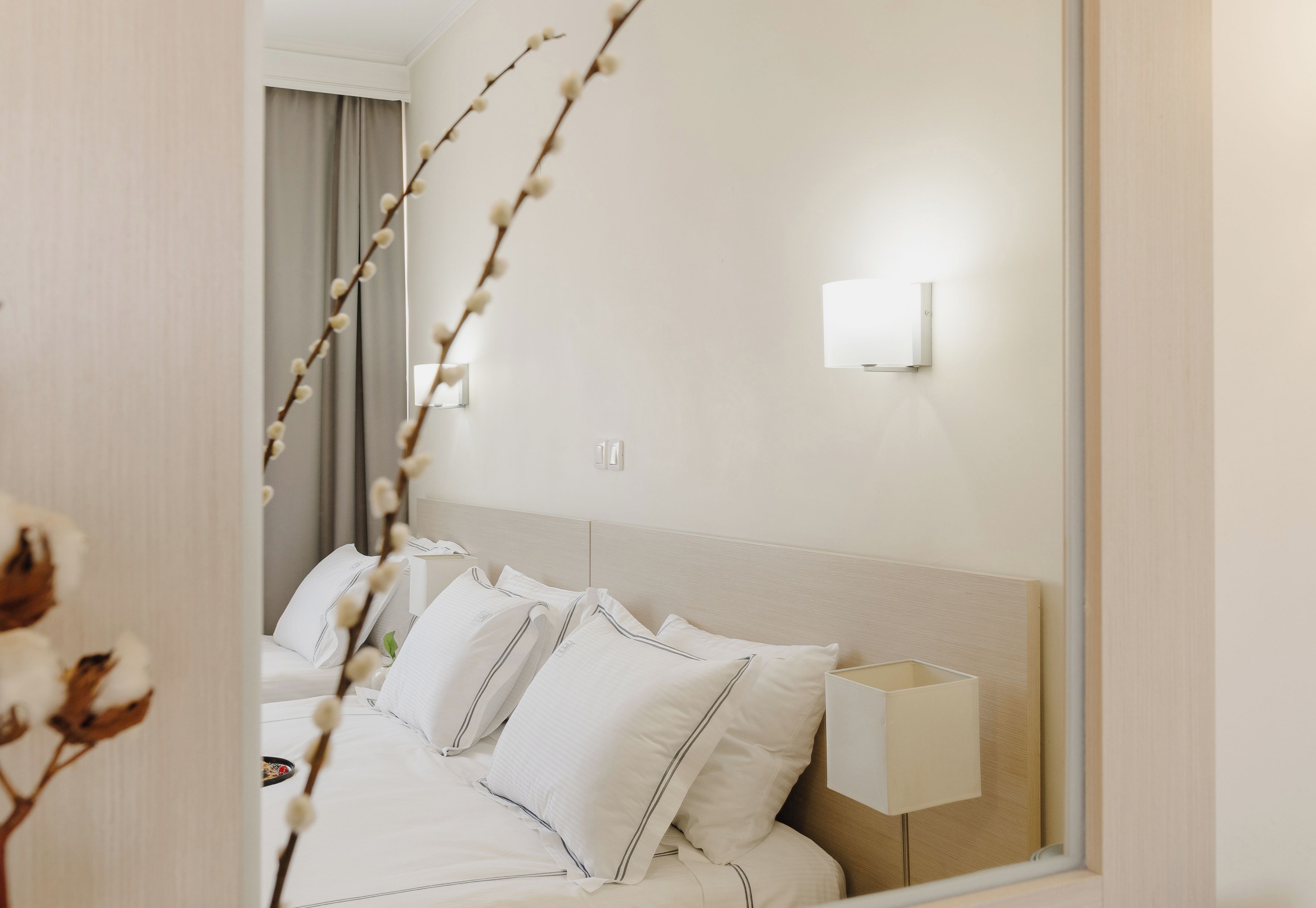 Habitación de hotel con cama, almohadas, lámpara de noche y un espejo que refleja parte de la habitación.