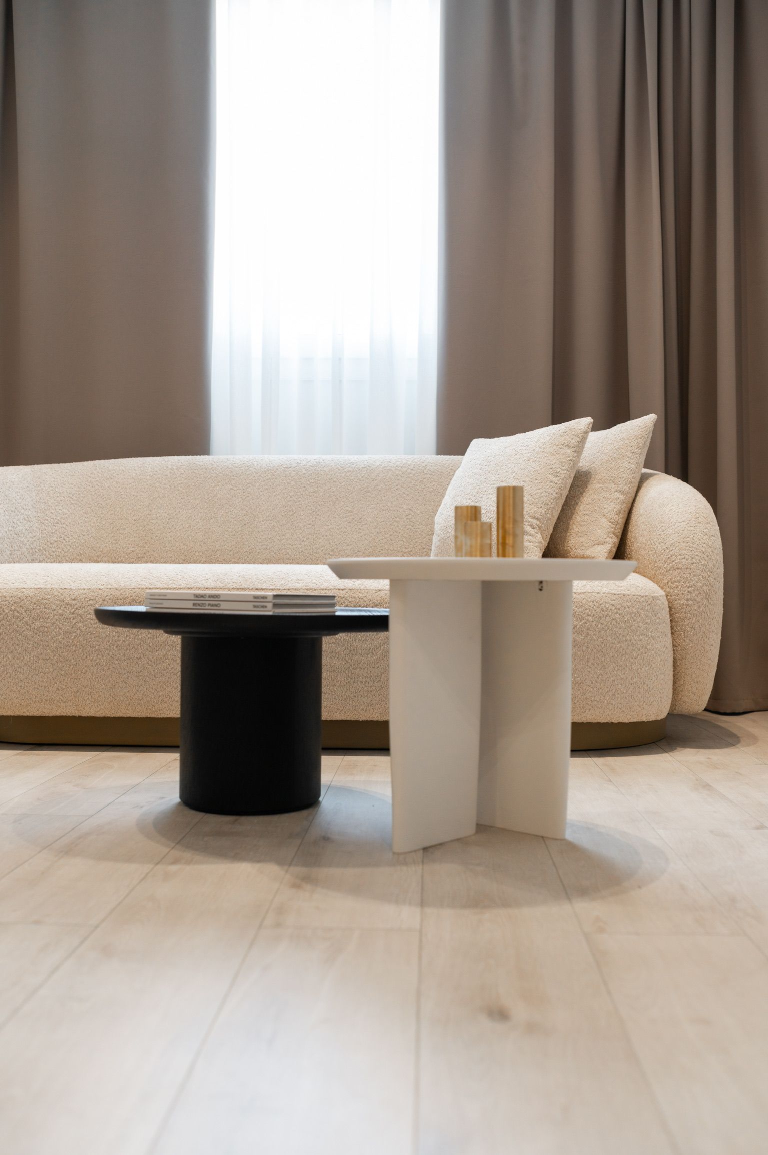 A modern living room with a beige sofa, a black and white coffee table, and a large window with curtains.