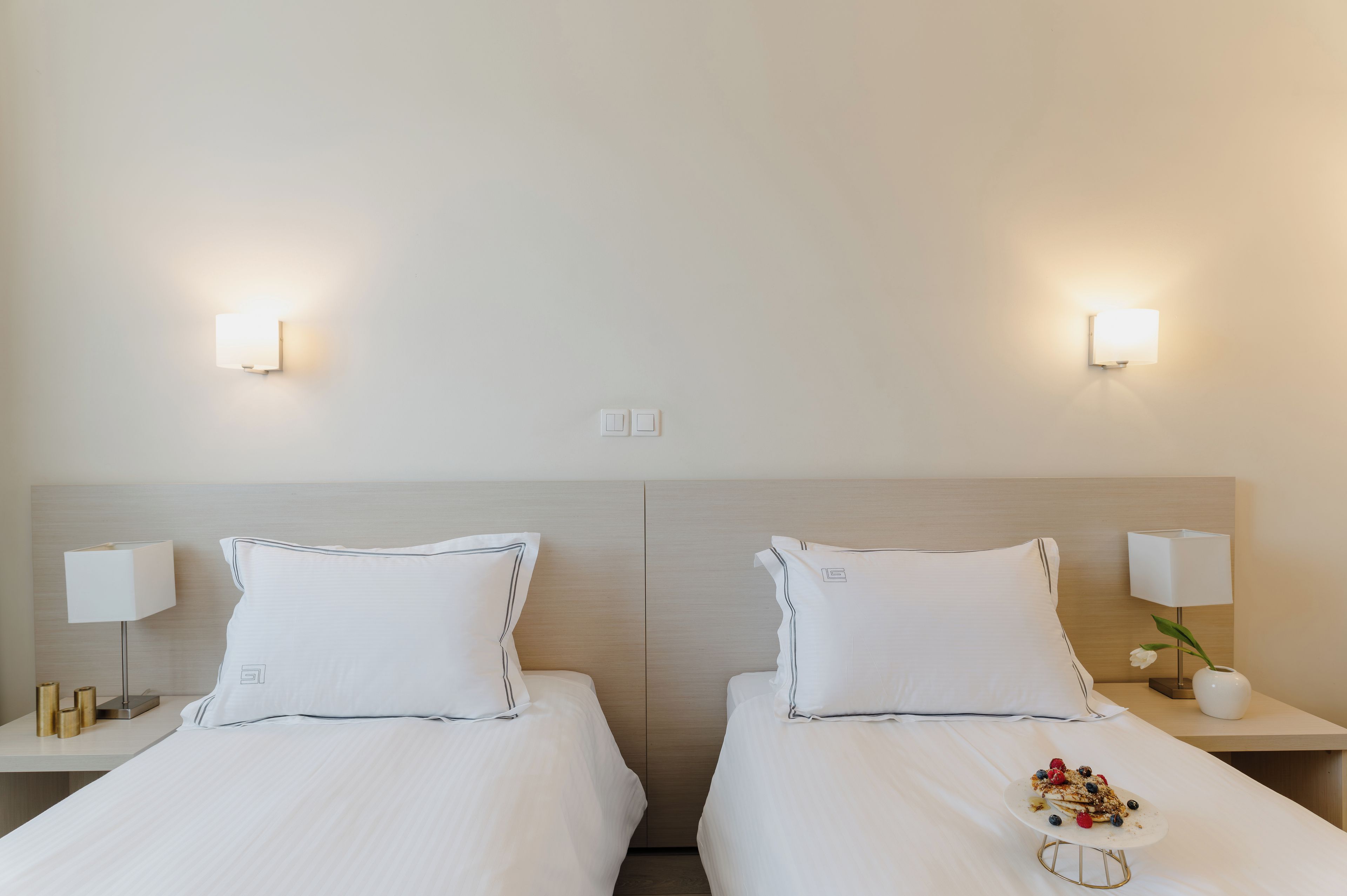 A hotel room with two beds, bedside tables with lamps, and a small table with a plate of food.