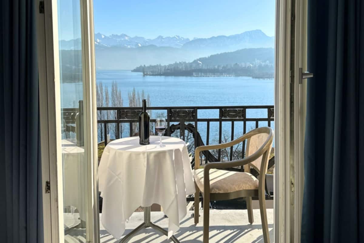 Un balcon avec une table et une chaise, donnant sur un lac et des montagnes.