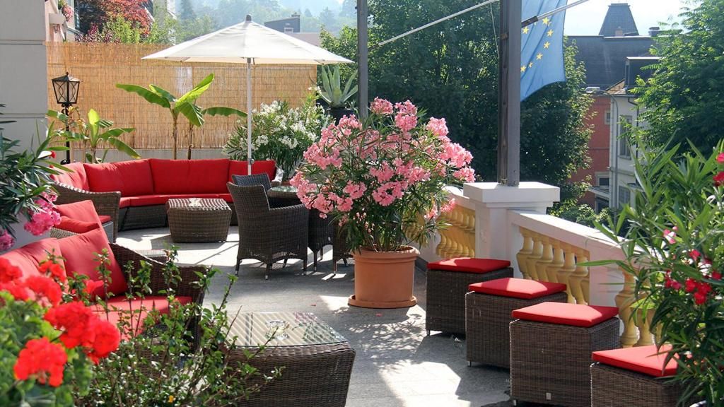 Eine Terrassengruppe im Freien mit Korbmöbeln, einem roten Sofa und Topfpflanzen.