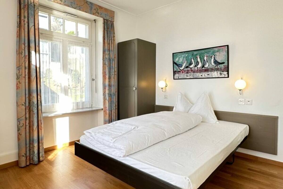 Une chambre à coucher avec un lit, une armoire, un tableau et une fenêtre avec des rideaux.