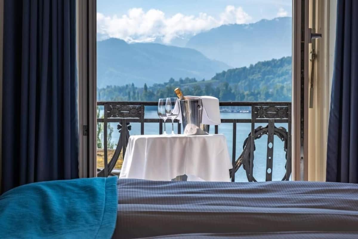 Un balcon avec une table dressée pour deux personnes, offrant une vue sur un lac et des montagnes.